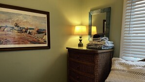 Une chambre à coucher avec un lit, une commode, une lampe, un miroir et un tableau accroché au mur.