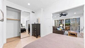 A bedroom with a large bed, a wardrobe, a dresser, and a sliding glass door leading to a living area with a sofa and a coffee table. - Sacred Cove Oasis - Indian Wells Tennis and Festival Hideaway (Indian Wells)