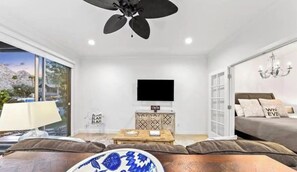 Una sala de estar moderna con una televisión de pantalla plana, un ventilador de techo, una araña y un sofá con cojines decorativos.