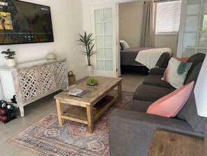 Una sala de estar con sofá, mesa de centro y televisor montado en la pared.