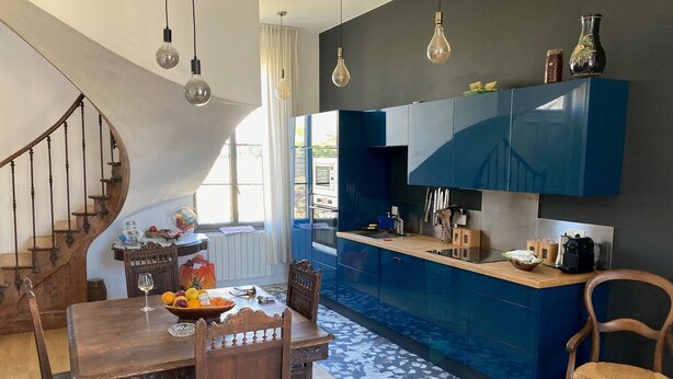 Une cuisine moderne avec des meubles bleus, une table à manger en bois et un escalier.