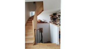 Un escalier en bois mène à un niveau inférieur, et une bibliothèque se trouve sur le côté droit.