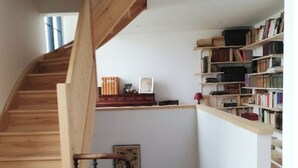 Un escalier en bois mène à un niveau inférieur, et une bibliothèque se trouve sur le côté droit.