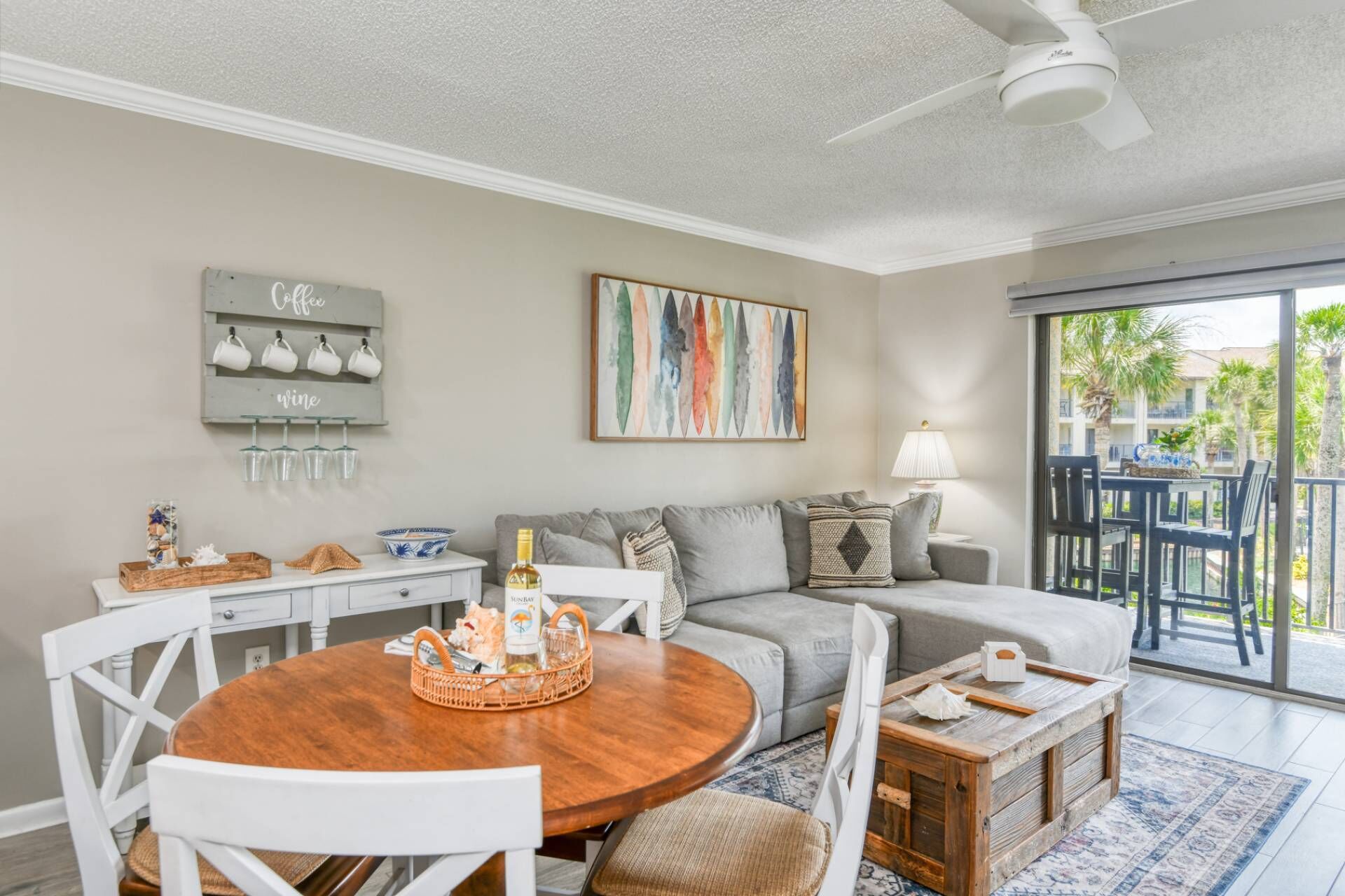 A living room with a wooden dining table, grey sofa, and a balcony with outdoor seating.