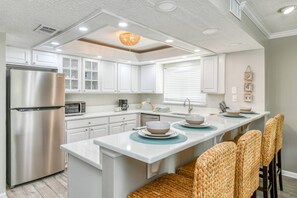 Uma cozinha moderna com armários brancos, eletrodomésticos de aço inoxidável e uma ilha central com lugares para sentar.
