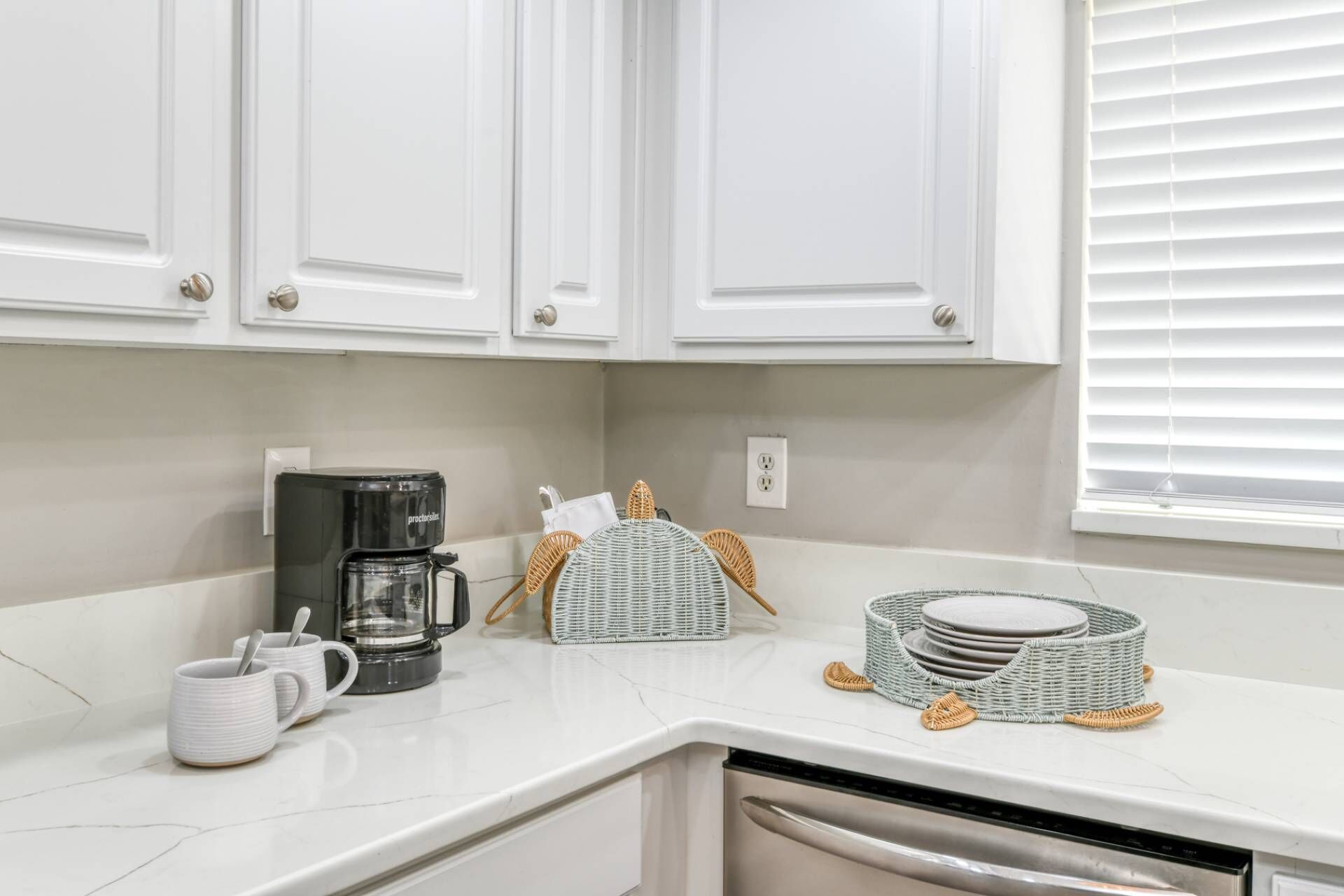 A kitchen with white cabinets, a coffee maker, a basket, and a dish rack.