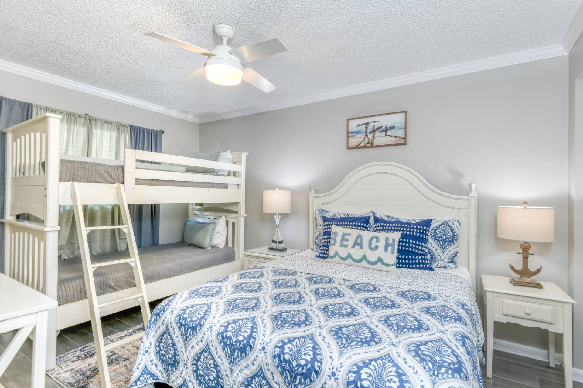 Une chambre avec des lits superposés, un lit recouvert d’une couvre-lit à motifs bleus, deux lampes de chevet et un ventilateur de plafond.