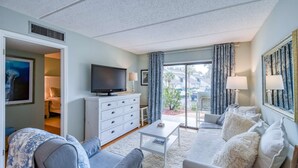 A modern living room with a flat-screen TV, white furniture, and a view of the outside. - Ocean and Racquet #3116 (St. Augustine)