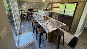 A modern kitchen with a large island, wooden cabinets, and a stainless steel refrigerator. - Modern lakeside private home, dock, main channel views, off Horsehoe Bend! (Lake Ozark)