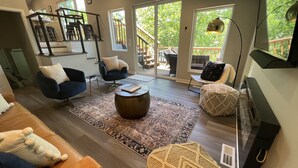 A spacious living room with a large window, a staircase, and a cozy seating area. - Modern lakeside private home, dock, main channel views, off Horsehoe Bend! (Lake Ozark)