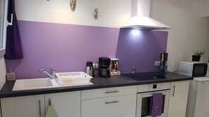 Een moderne keuken met een paars achterspiegeltje, witte kastjes, een ingebouwde oven en een koffiezetapparaat.