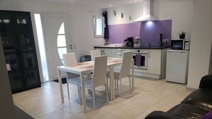 Een moderne keuken met witte kasten, een eettafel met vier stoelen en een zwarte leren bank in de woonkamer.