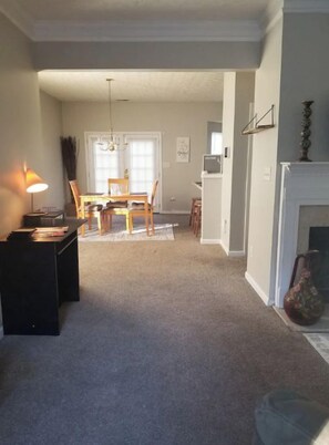 A spacious living room with a carpeted floor, a dining area with a wooden table and chairs, and a fireplace.