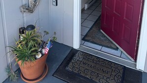 A house entrance with a red door, a welcome sign, a mailbox, and a potted plant.