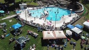 A large outdoor swimming pool surrounded by grassy areas and picnic tables.