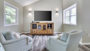 A living room with a large flat-screen TV mounted on the wall, a wooden entertainment center, and two striped armchairs.