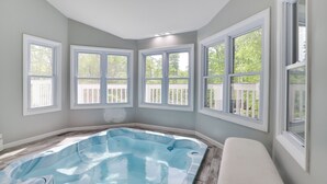 A spa room with a hot tub, large windows, and a view of the outside deck.