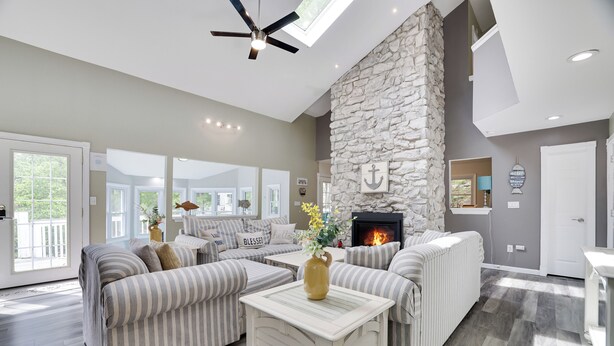 A spacious living room with a stone fireplace, striped sofas, and a ceiling fan.