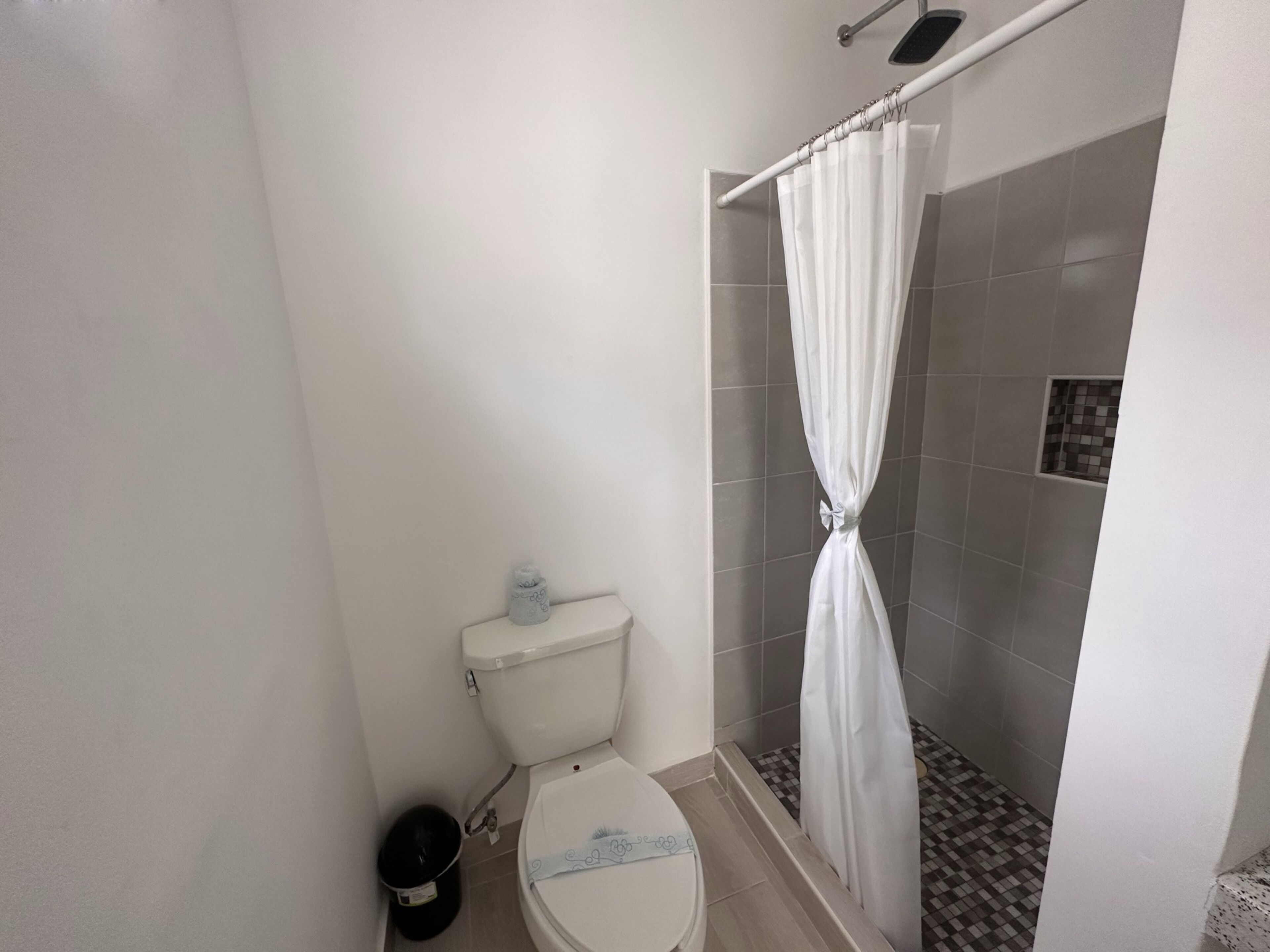 A bathroom with a toilet, a shower with a curtain, and a tiled floor.
