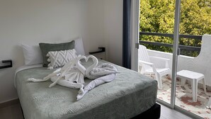 Habitación de hotel con cama, ventana con vista a la vegetación y puerta corrediza de vidrio que da a un espacio exterior con sillas.