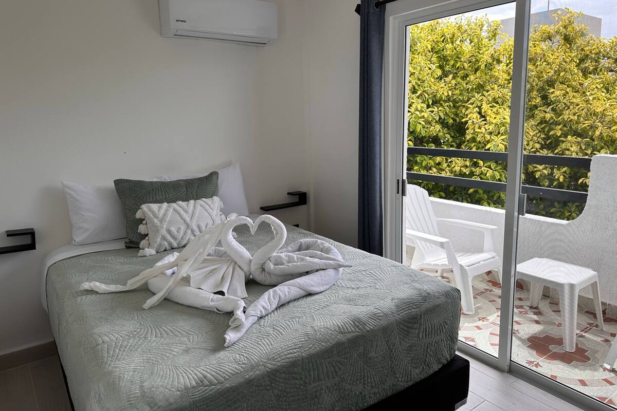 Hotelkamer met een bed, een raam met uitzicht op groen en een schuifdeur die leidt naar een buitenruimte met stoelen.