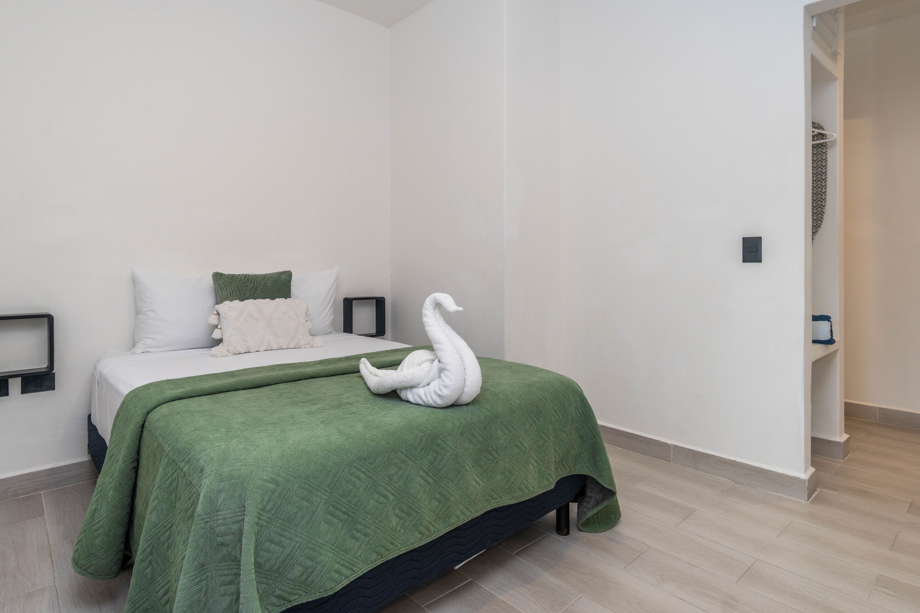A minimalist bedroom with a bed, green bedding, and a swan-shaped towel.