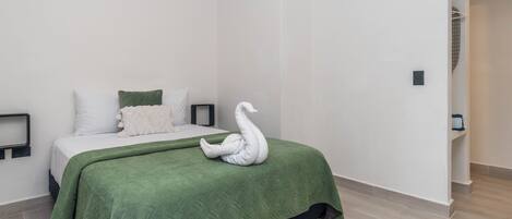 A minimalist bedroom with a bed, green bedding, and a swan-shaped towel.