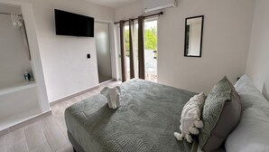 Un dormitorio moderno con una cama grande, un televisor de pantalla plana en la pared, una puerta corrediza de vidrio que da a un balcón y un aire acondicionado integrado.