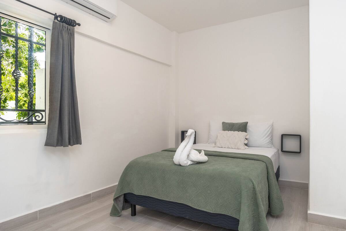 Een slaapkamer met een bed, een raam met gordijn en een wandairconditioner.