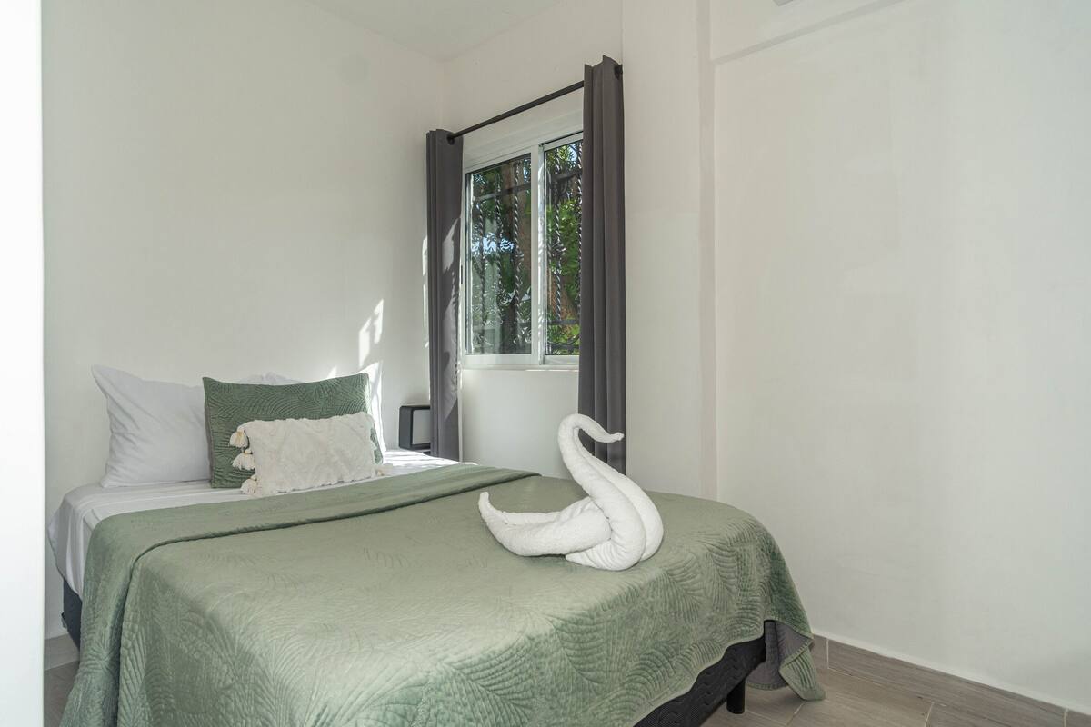 Een net opgemaakt bed met een groene deken en een handdoek in de vorm van een zwaan.