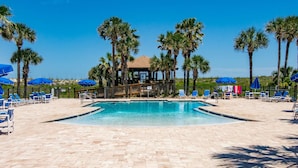 A pool area with lounge chairs and umbrellas, surrounded by palm trees. - Ocean Villas #76 (St. Augustine)