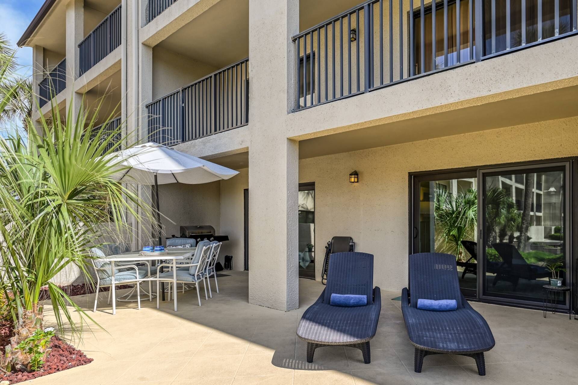 Een balkon met twee loungestoelen, een tafel met stoelen en een barbecue.