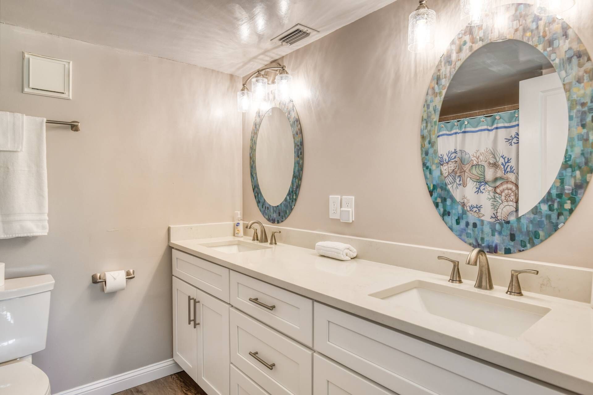 Une salle de bain avec deux lavabos, des toilettes et un grand miroir agrémenté d’un cadre décoratif.