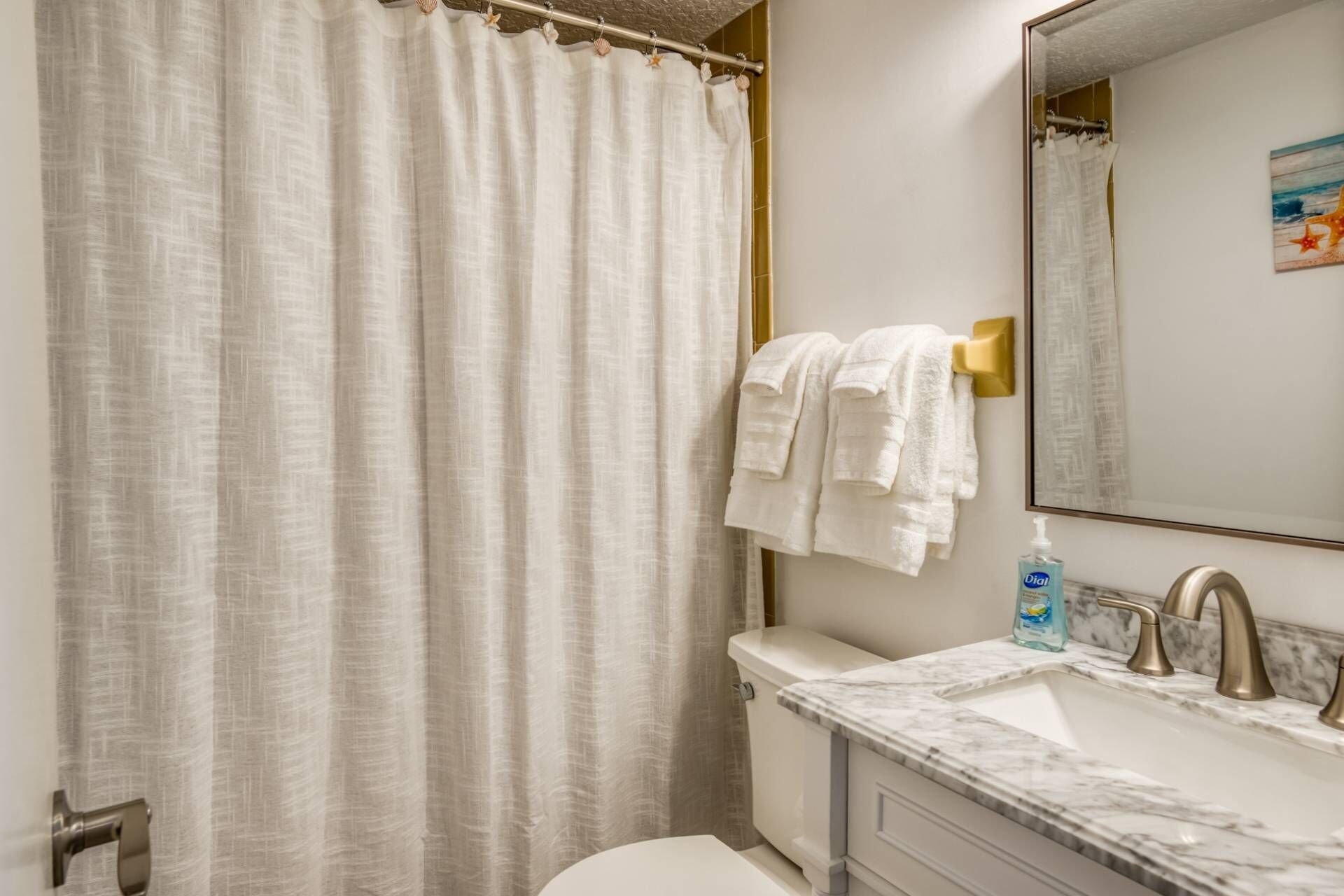 A bathroom with a white shower curtain, a white toilet, a marble sink with gold faucets, and a towel rack with white towels.