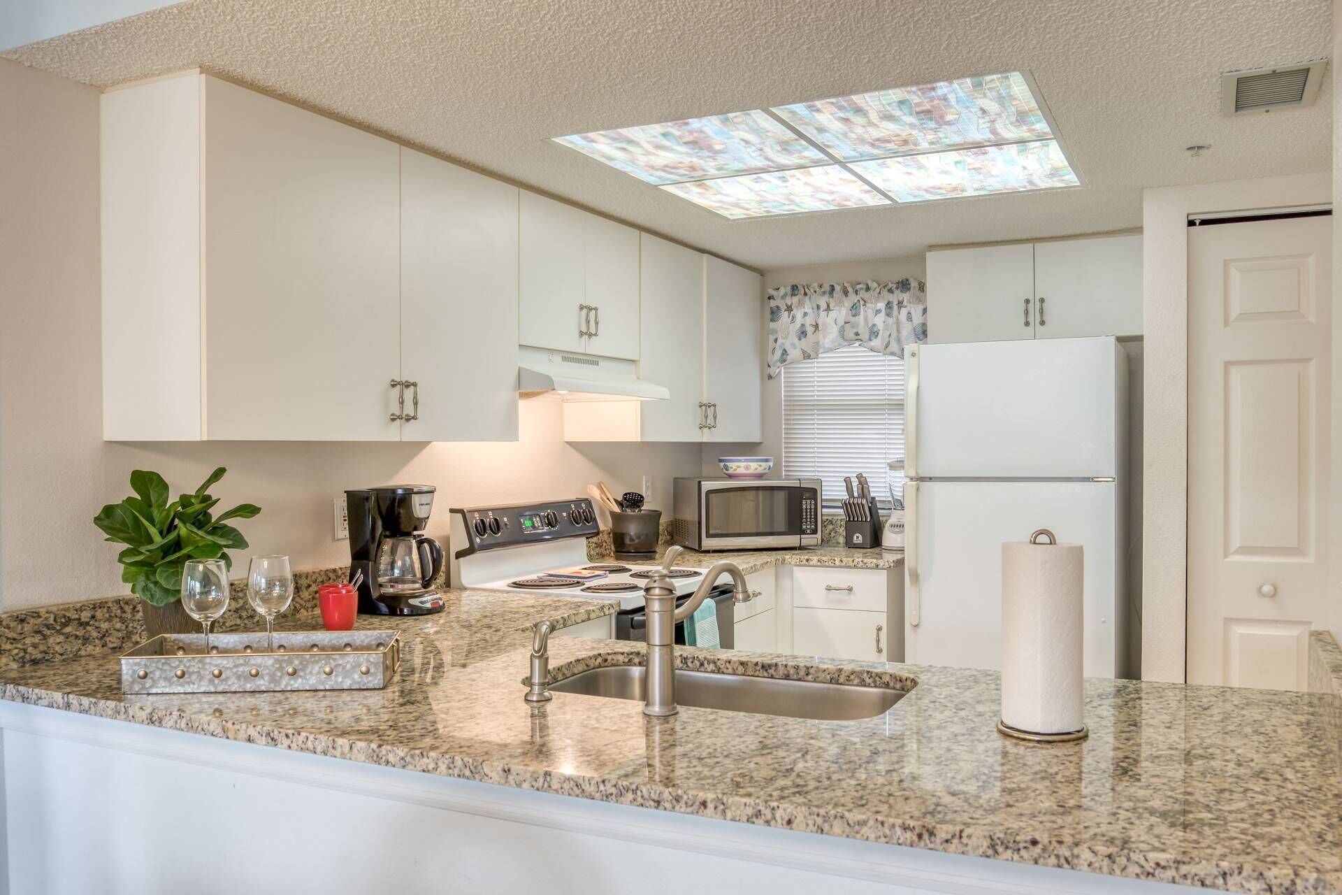 Una cocina con gabinetes blancos, encimera de granito, pileta de acero inoxidable, microondas, estufa y refrigerador.