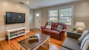 A living room with a flat-screen TV, a leather couch, a wooden coffee table, and a grey sofa. - Bleu Daze Cottage (St. Augustine)