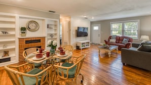 A living room with a fireplace, a TV, a dining area with wicker chairs, and a sofa. - Bleu Daze Cottage (St. Augustine)