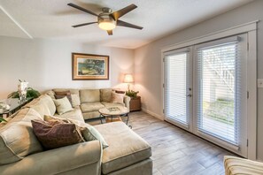 A living room with a sectional sofa, a round coffee table, a ceiling fan, a lamp, and a painting on the wall. - Flagler Flat (St. Augustine)