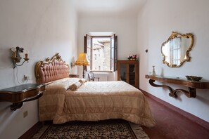 A bedroom with a large bed, a nightstand, a lamp, a mirror, and a view through a window.
