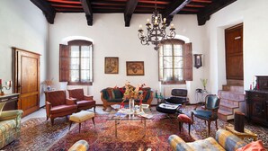 A traditional living room with a high ceiling, wooden beams, a chandelier, and a variety of seating including armchairs and sofas. - San Gimignano Dependance Rose's Rooms, with 4 rooms, full center, fast WiFi. (San Gimignano)
