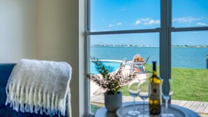 A view from a window overlooking a pool area with a chair and table set up for dining, and a bottle of wine on the table. - Porpoise Point (St. Augustine)