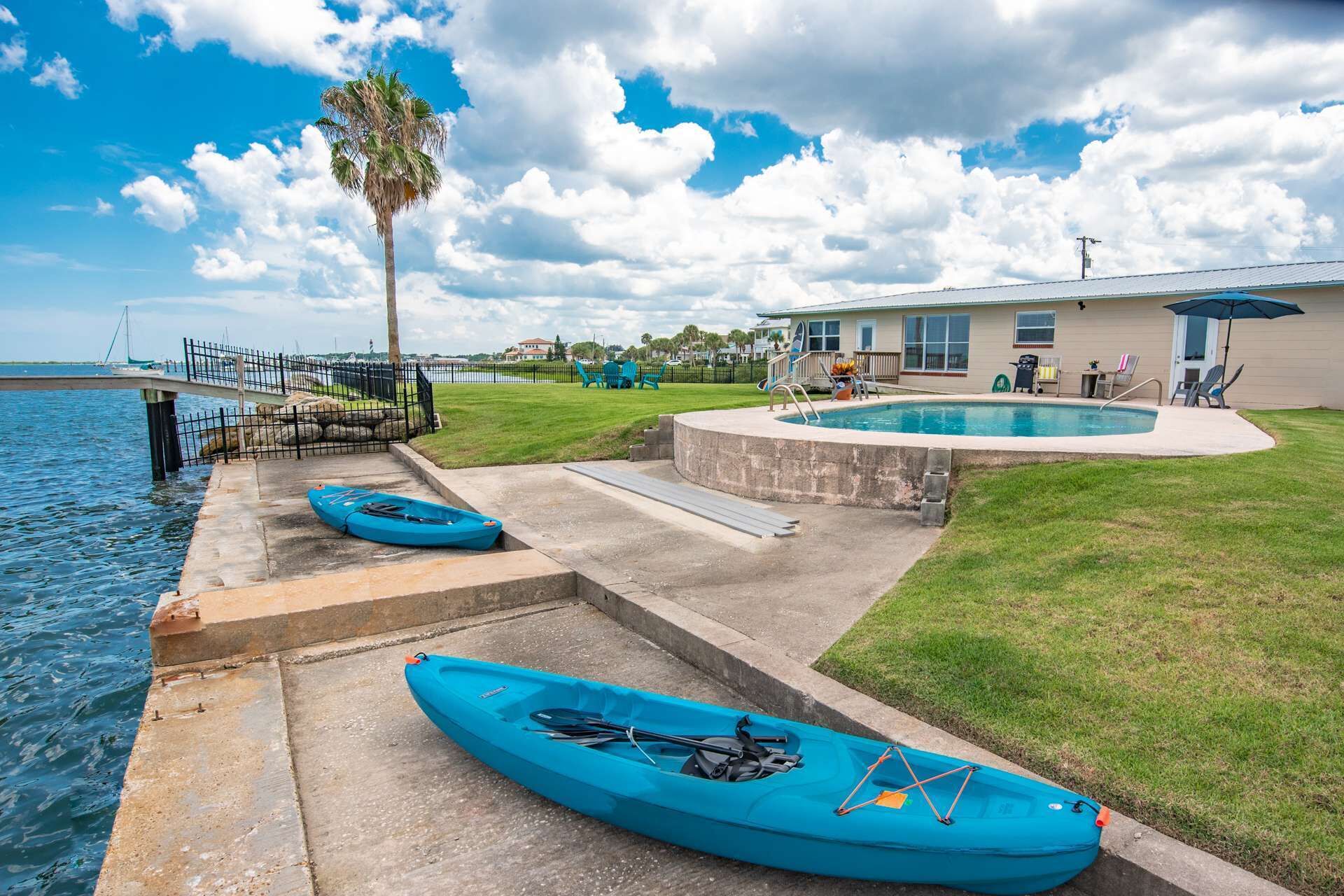 A waterfront property with a swimming pool, kayaks, and a dock.