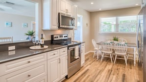 A modern kitchen with white cabinetry, a stainless steel stove, and a dining area with white chairs. - Porpoise Point (St. Augustine)