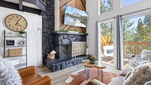 A modern living room with a fireplace, a large clock, and a scenic view through the glass door.