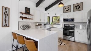 A modern kitchen with white cabinets, a large island with bar stools, a built-in oven, and a hanging pendant light.