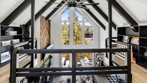 A loft-style room with a sloped ceiling, exposed beams, and a large window offering a view of the outdoors.