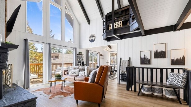 A spacious living room with a fireplace, a high ceiling, and a large window overlooking a deck.