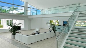 Amplia sala de estar con un sofá seccional blanco grande, una escalera de cristal y vistas al exterior.