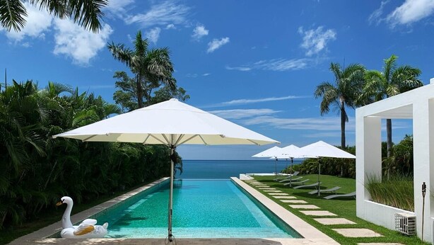 Una piscina con sillones reclinables y sombrillas, rodeada de vegetación y vistas al océano.