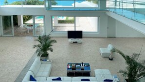 Un amplio salón con un televisor grande, sofás blancos y vistas a la playa.